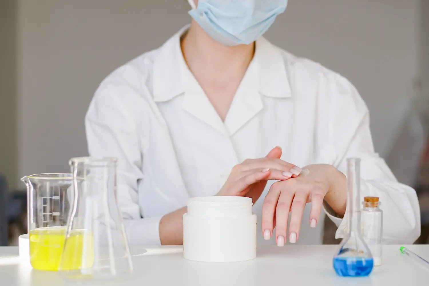 Skin expert in white lab coat applying moisturizer cream on her hand to test popular skin care products in the laboratory.